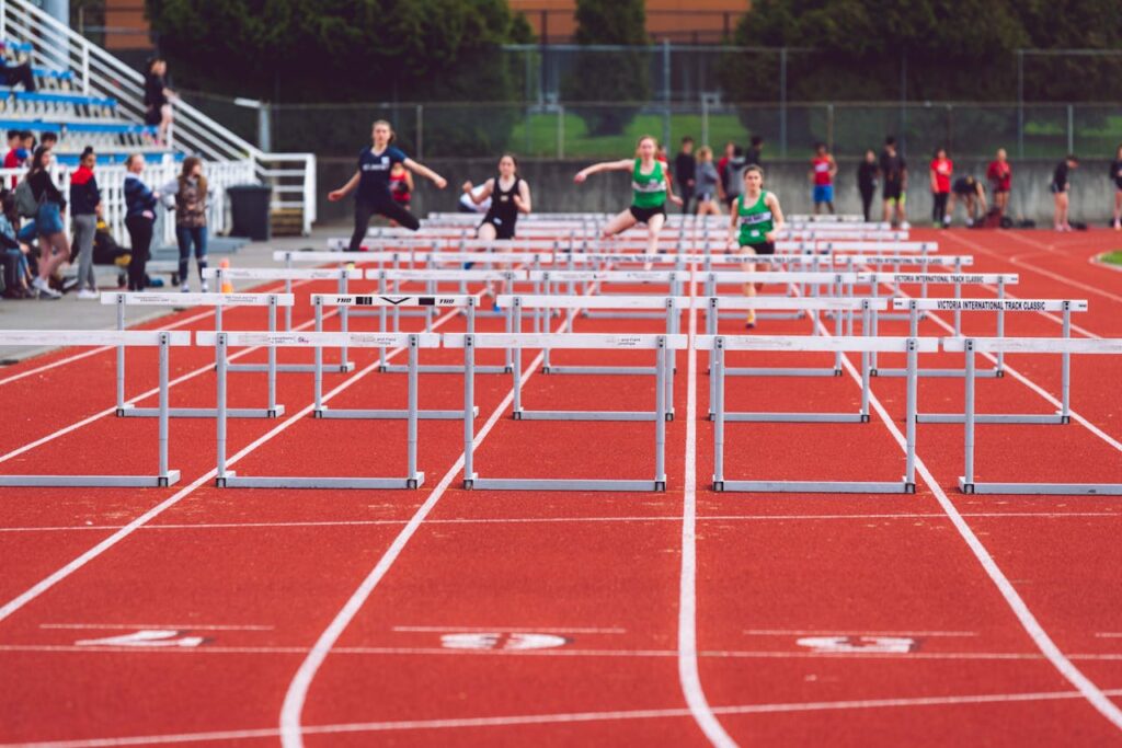 Women athletes compete in a hurdles race at a Victoria track event on a sunny day.